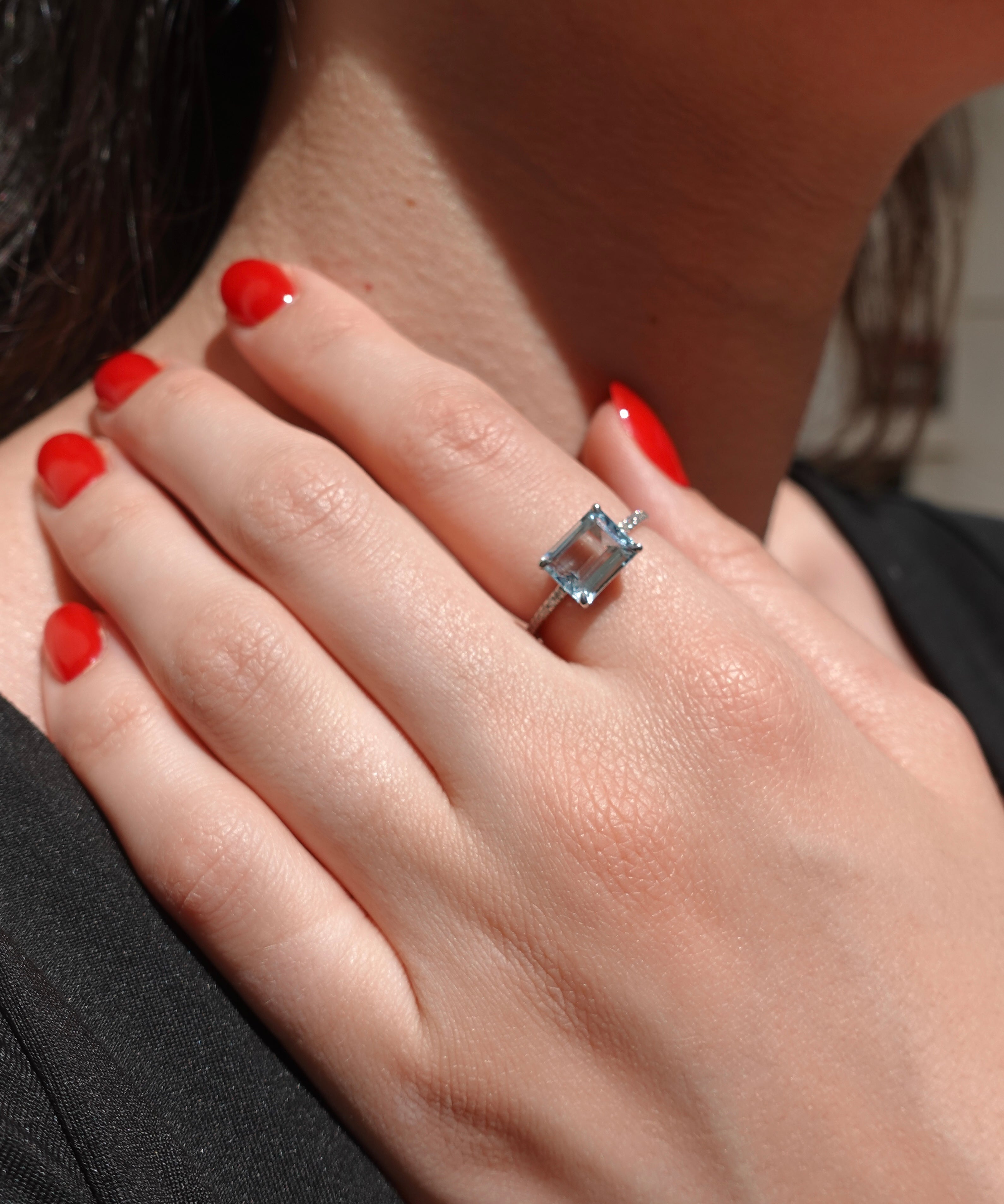 Close-up of a hand wearing a ring with a blue aquamarine gemstone, against a blurred background.