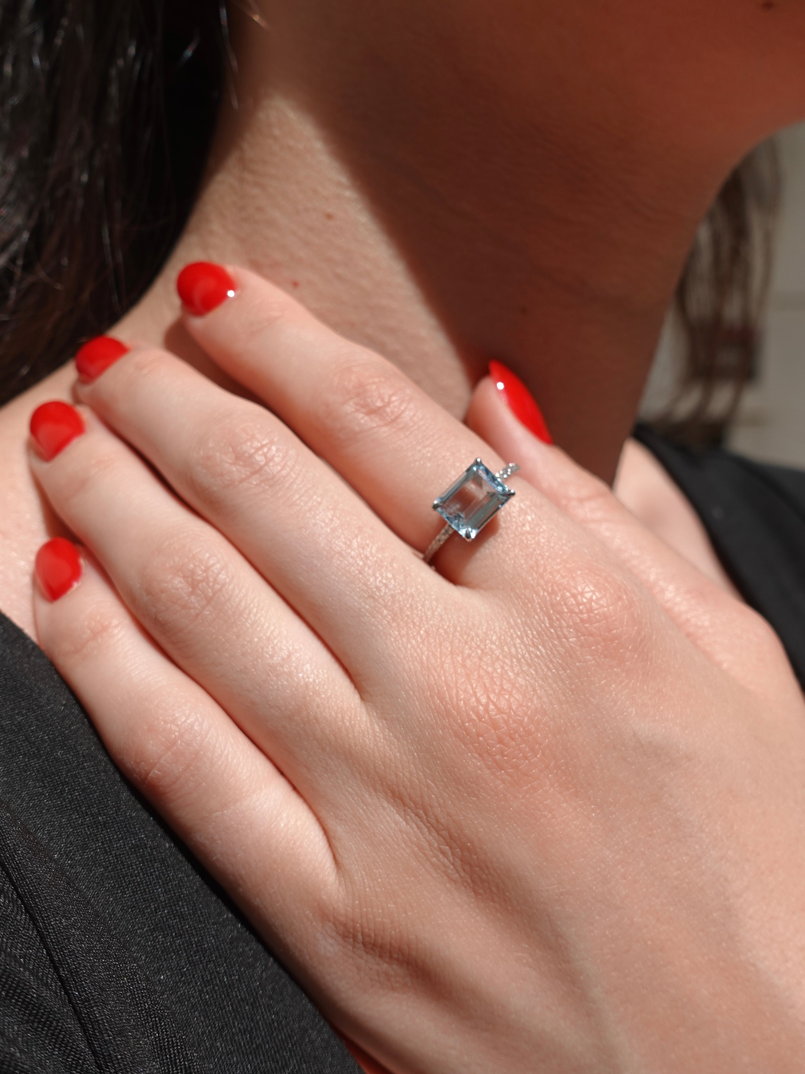 Close-up of a hand wearing a ring with a blue aquamarine gemstone, against a blurred background.