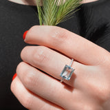Hand wearing a diamond ring with a blue gemstone, holding a bundle of grass against a black background.