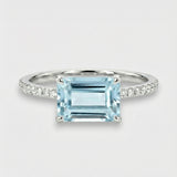 Ring with an emerald-cut aquamarine and diamond-studded band on a light gray background