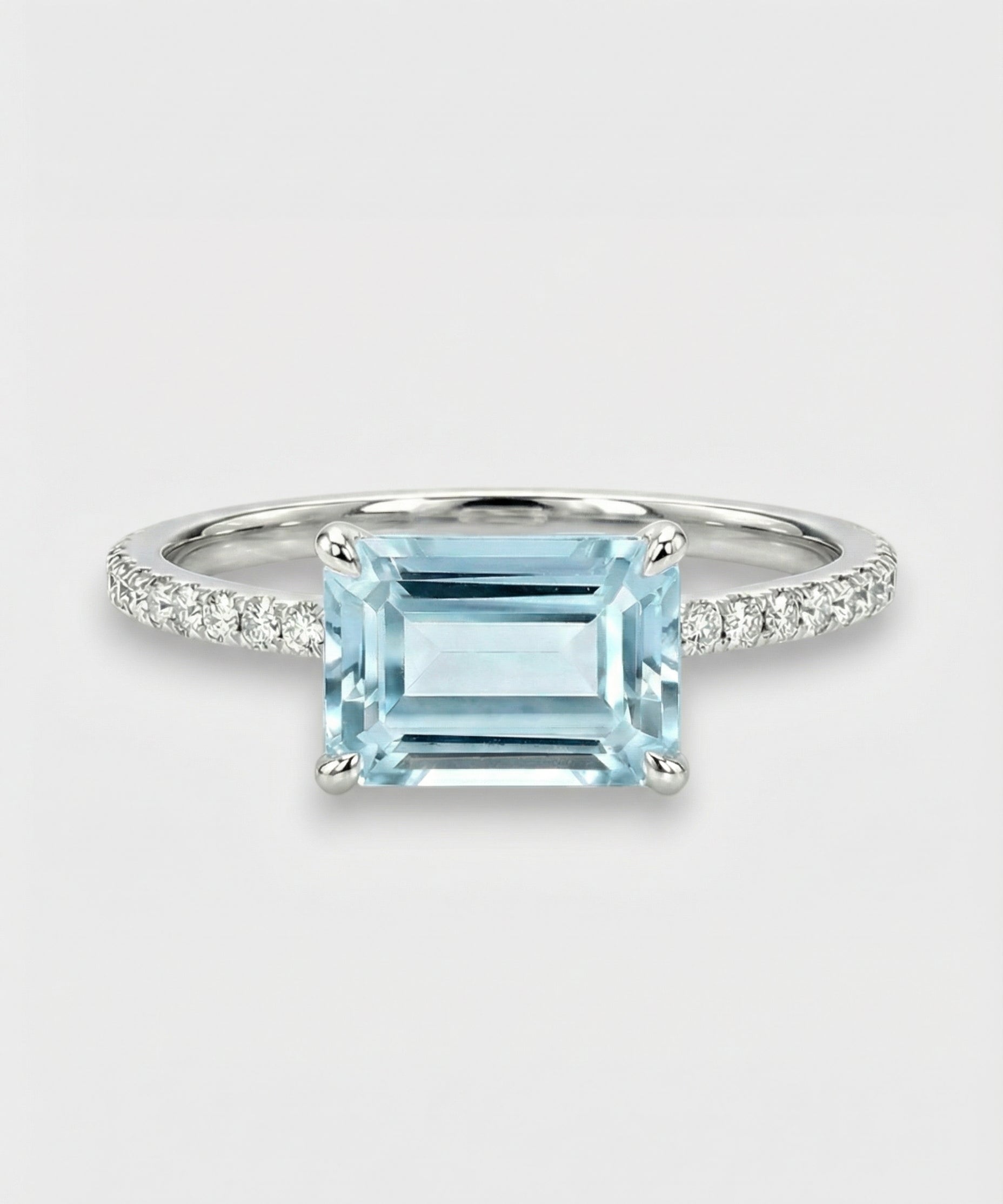 Ring with an emerald-cut aquamarine and diamond-studded band on a light gray background