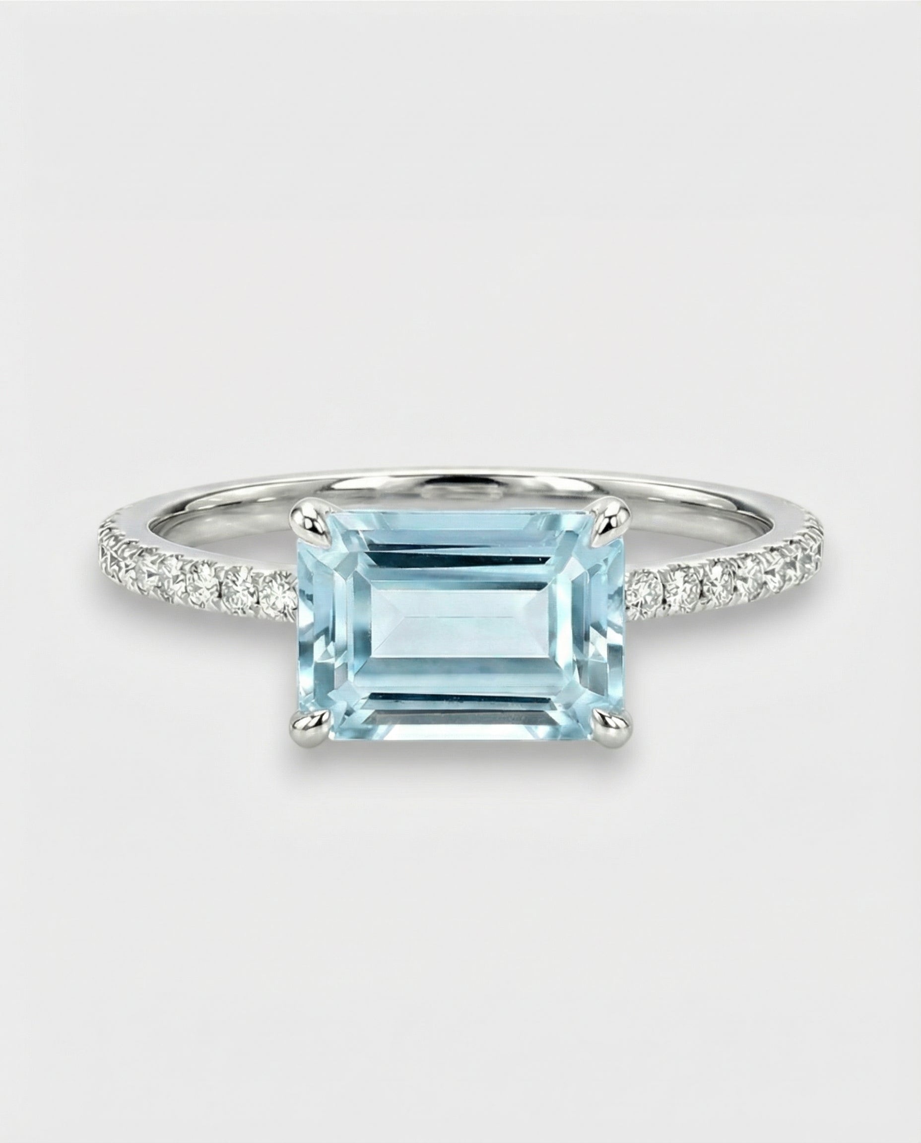Ring with an emerald-cut aquamarine and diamond-studded band on a light gray background