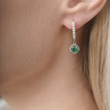 Close-up of a person wearing a green emerald gemstone earring.