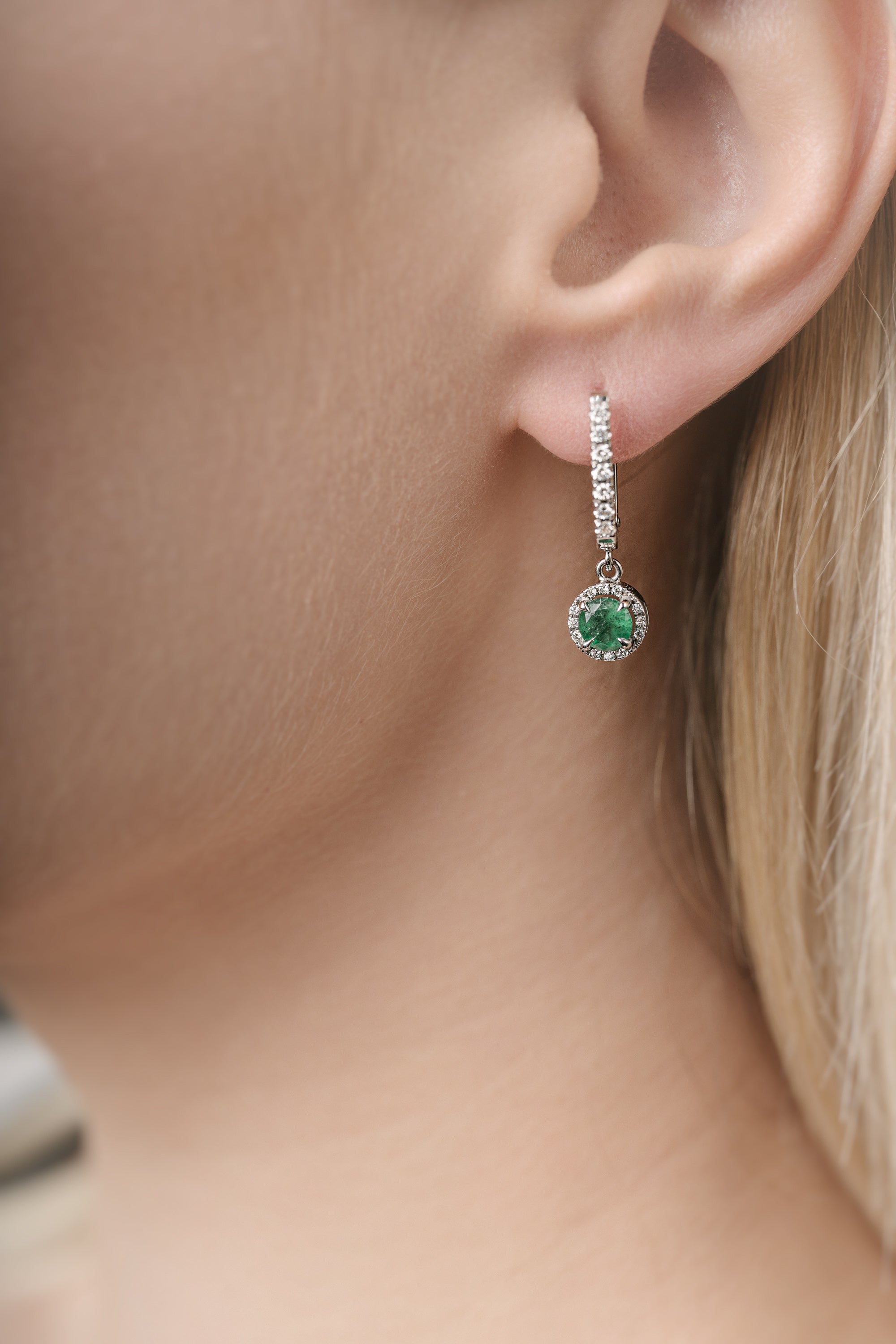 Close-up of a person wearing a green emerald gemstone earring.