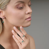 Woman wearing emerald green earrings and ring on a neutral background