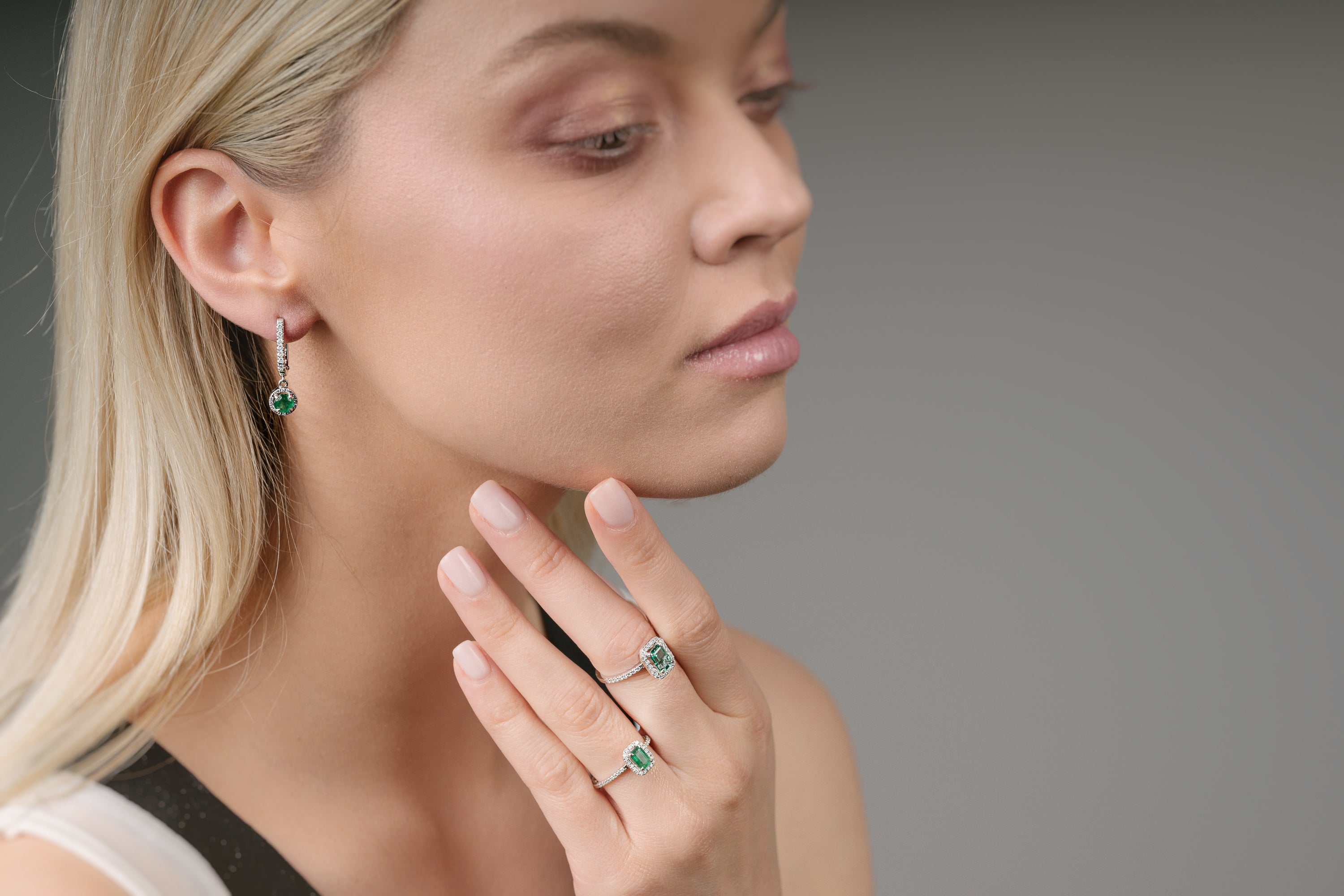 Woman wearing emerald green earrings and ring on a neutral background