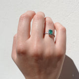 Hand wearing a ring with a green emerald gemstone on a light background