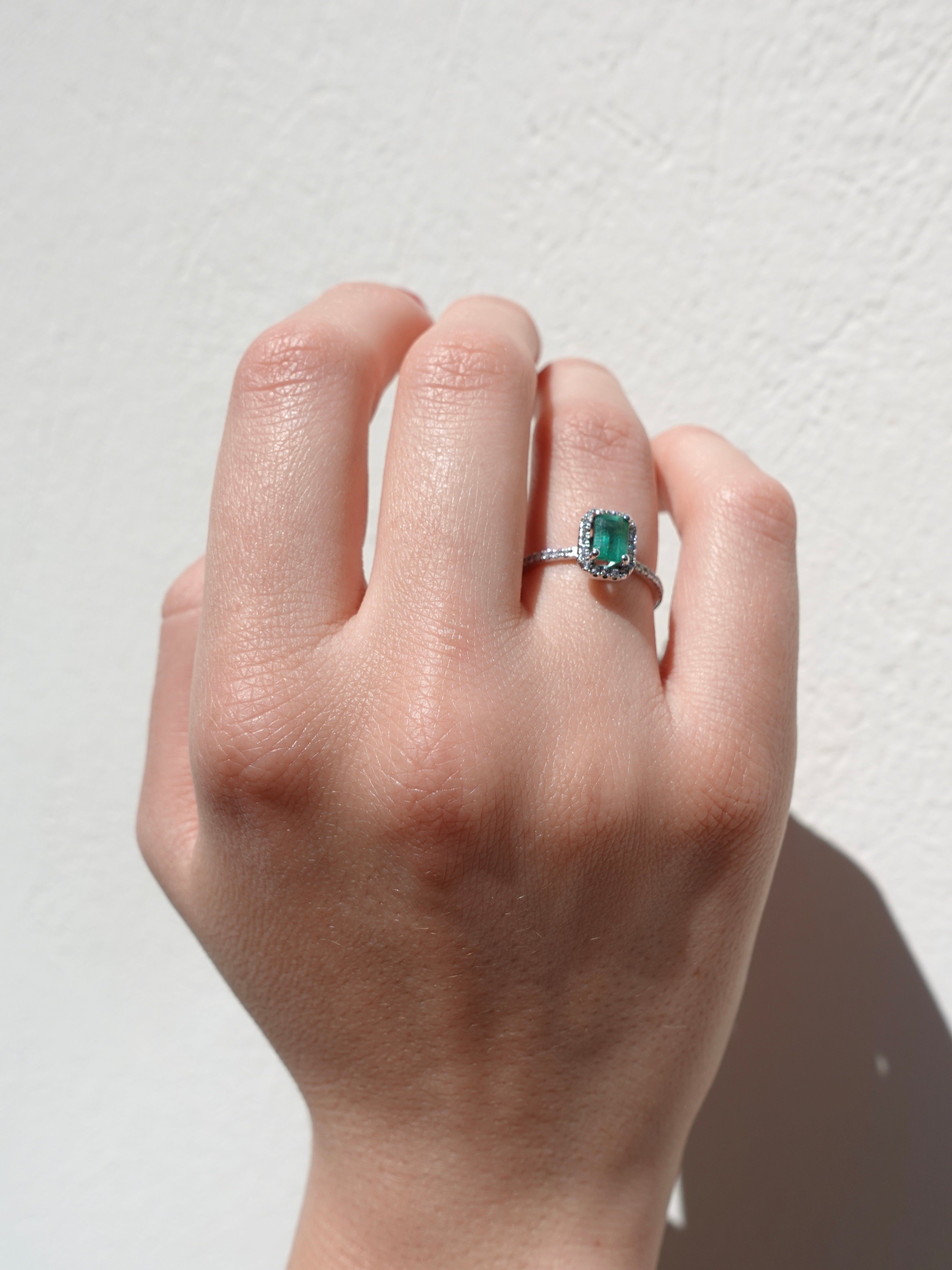Hand wearing a ring with a green emerald gemstone on a light background
