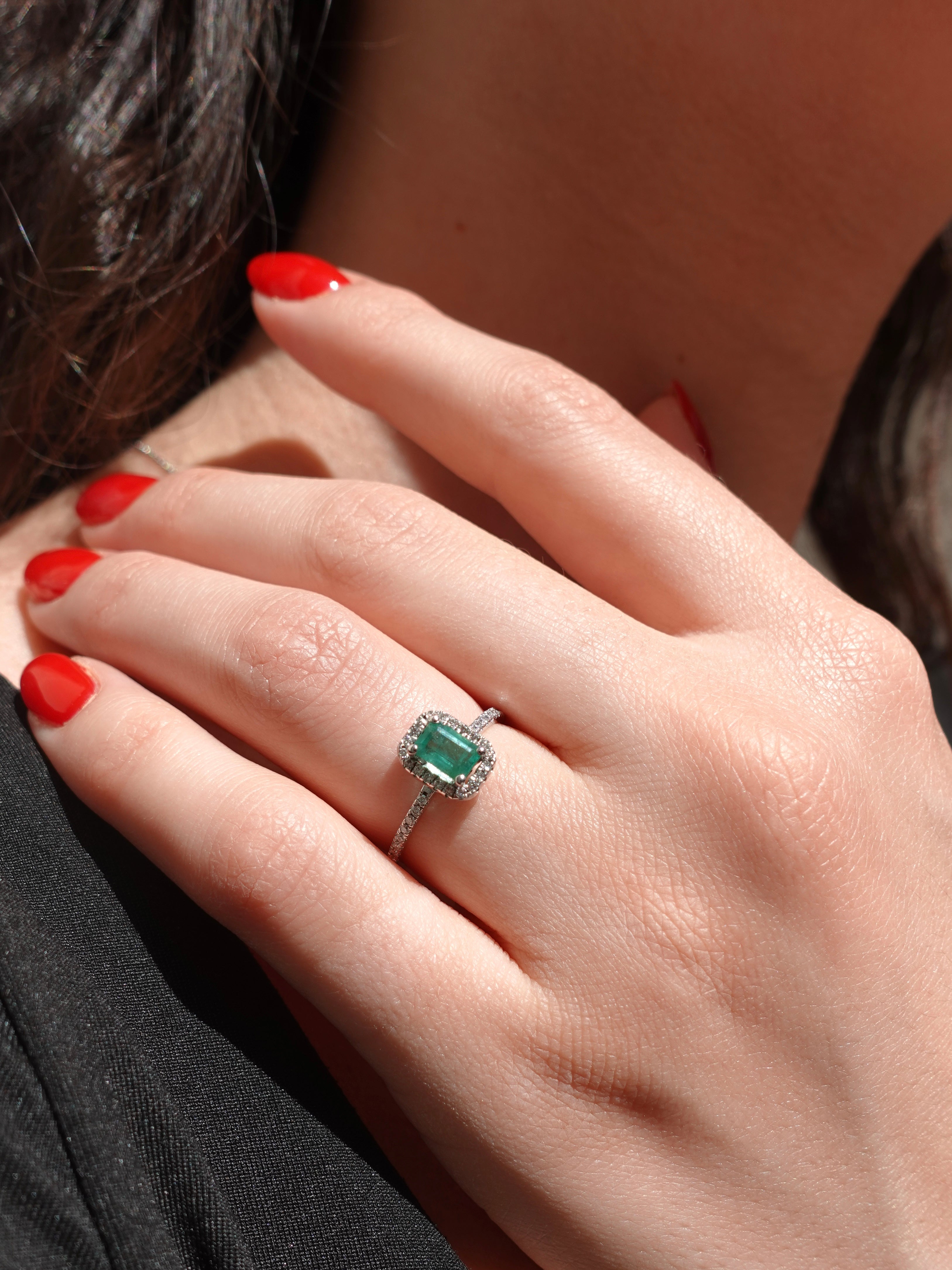 Close-up of a hand wearing an emerald ring with red nail polish.