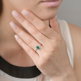 Close-up of a hand wearing a ring with an emerald and diamond halo, held near the face.