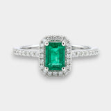 Emerald ring with diamond halo on a white background