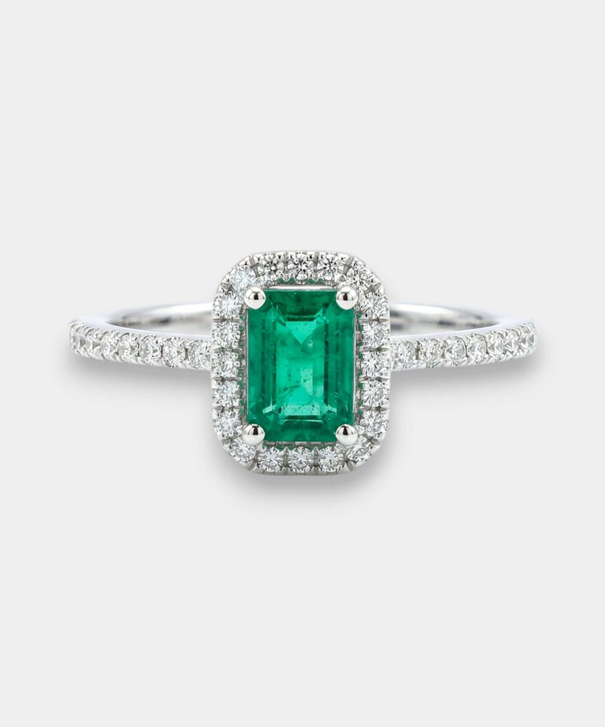 Emerald ring with diamond halo on a white background