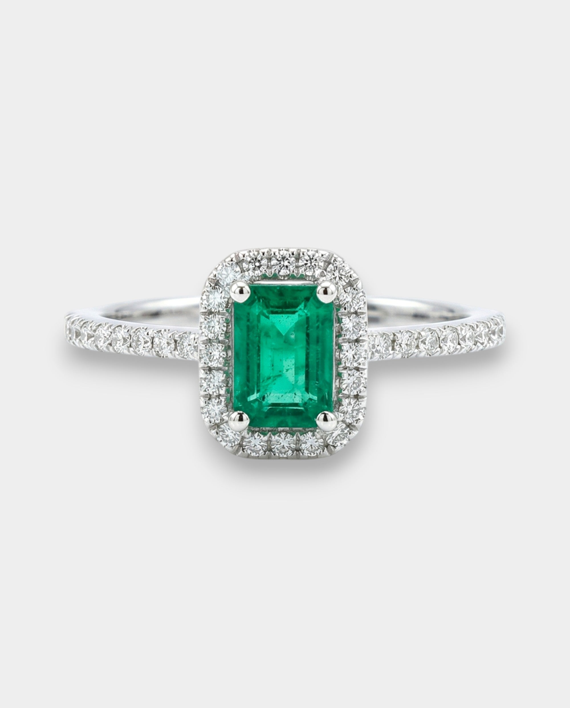 Emerald ring with diamond halo on a white background