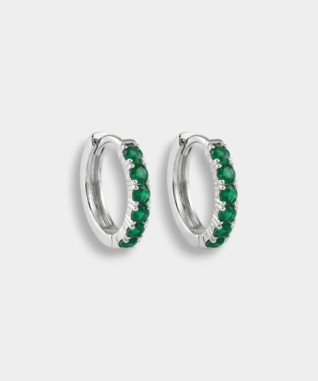 Pair of white gold hoop earrings with emeralds on a white background