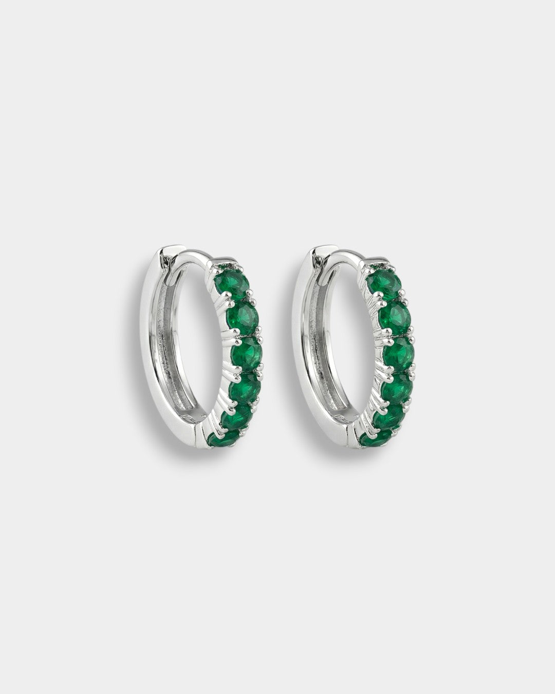 Pair of white gold hoop earrings with emeralds on a white background
