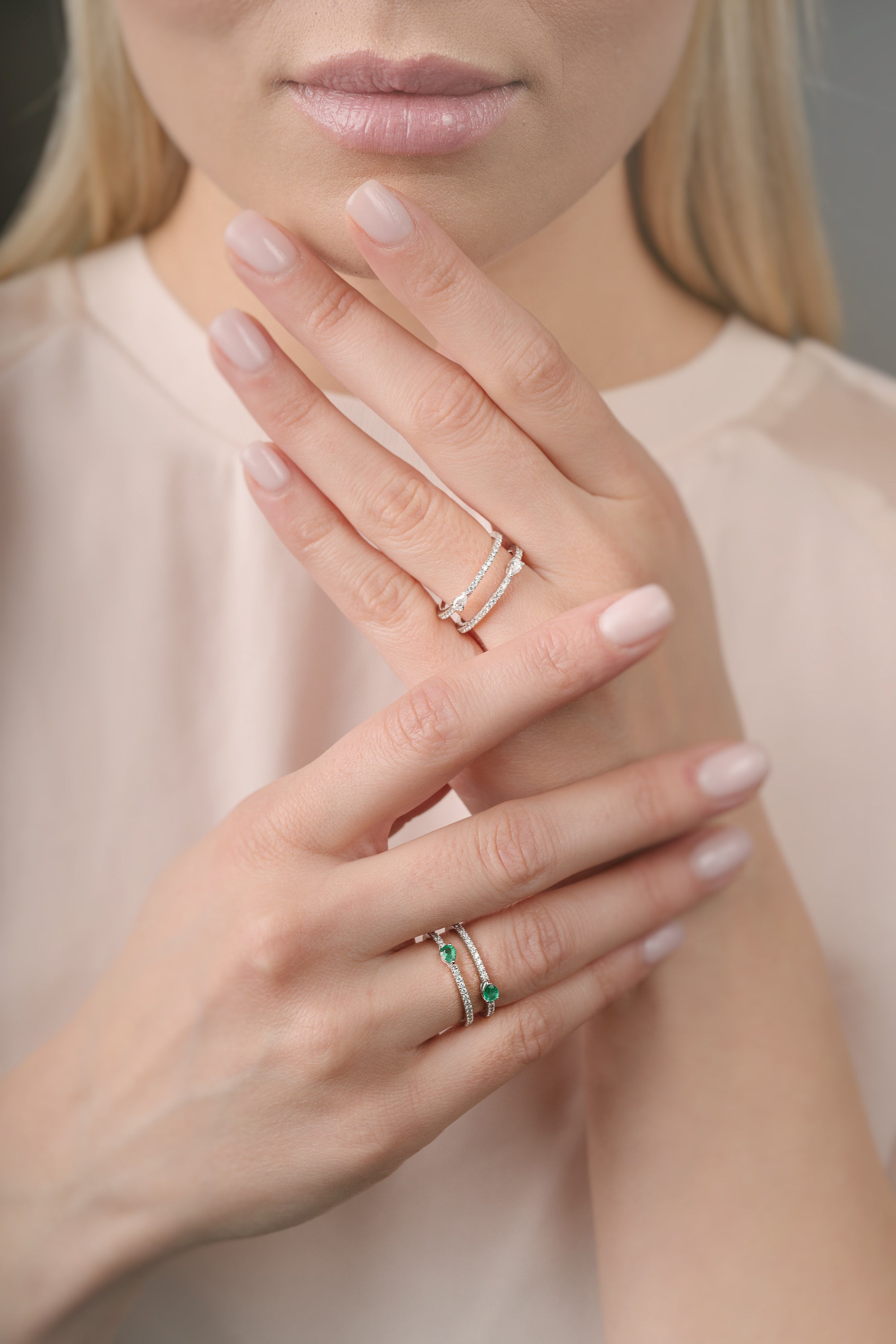 Close-up of a person's hands wearing multiple rings with a neutral background