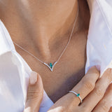 Necklace and ring with emerald stones worn by a person in a white shirt.