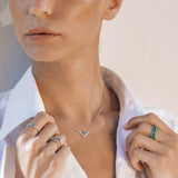 Woman wearing a necklace with a white shirt and multiple rings on a neutral background