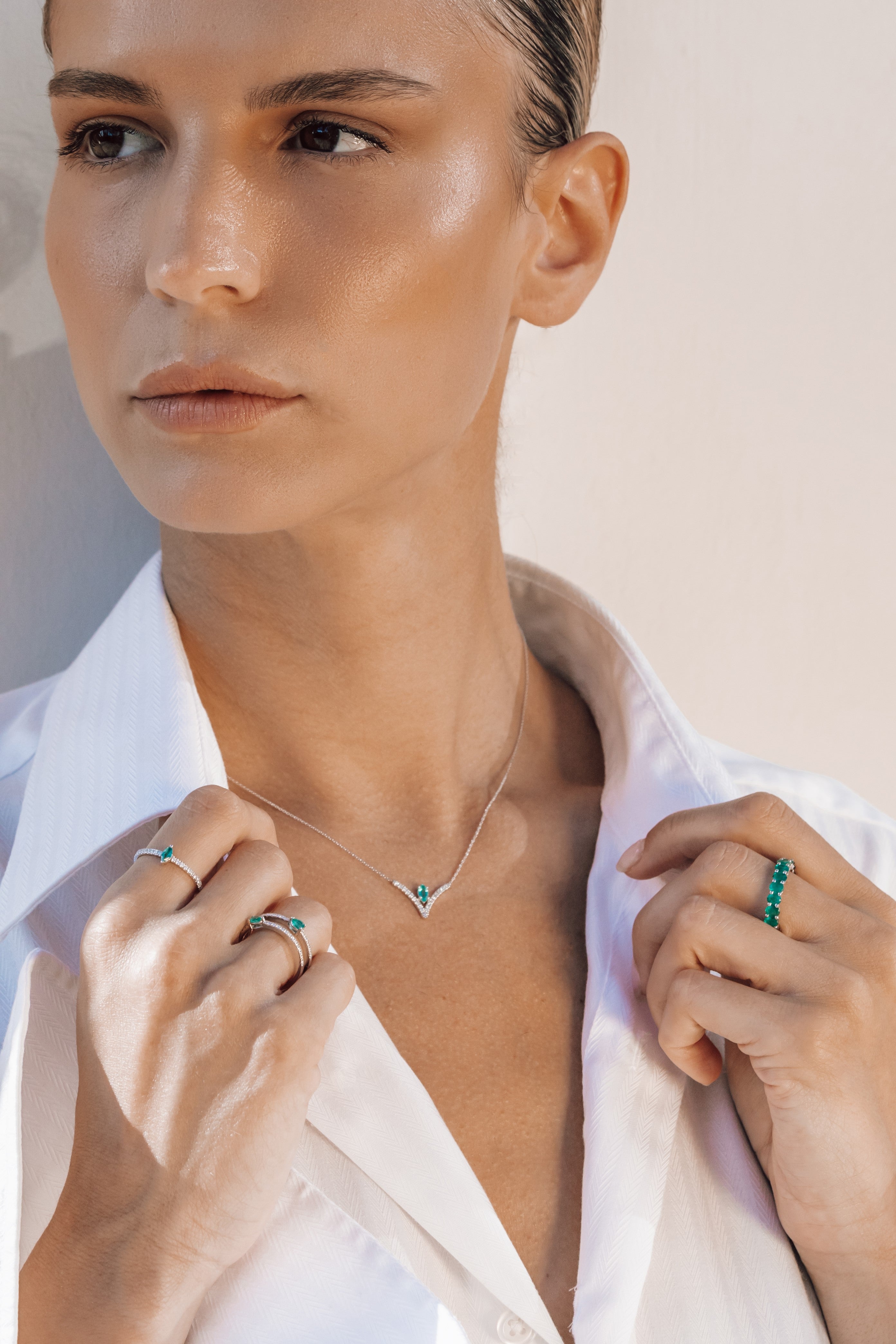 Woman wearing a necklace with a white shirt and multiple rings on a neutral background