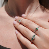 Close-up of a hand wearing two white gold rings with green gemstones on a blurred background