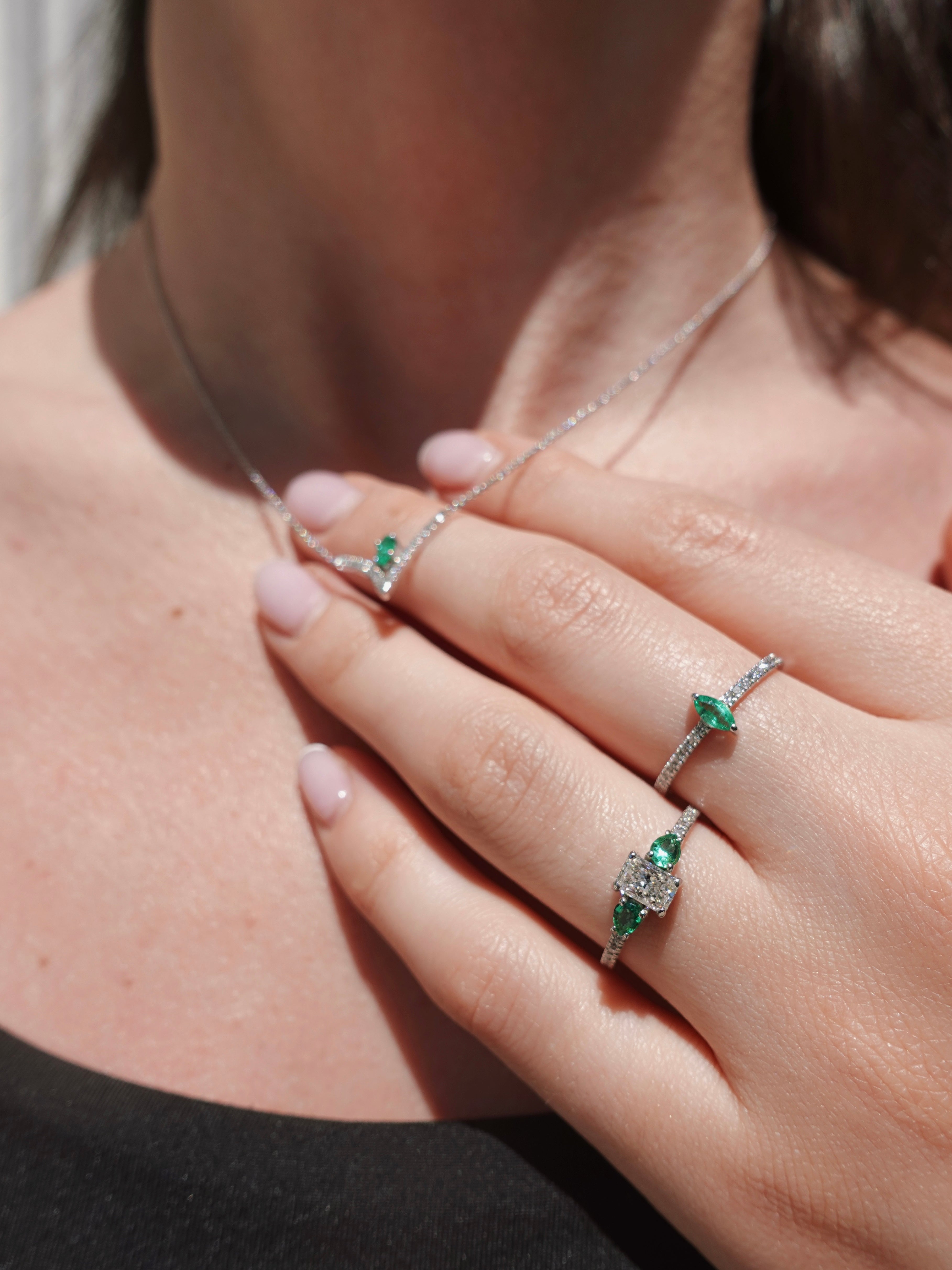 Close-up of a hand wearing two white gold rings with green gemstones on a blurred background