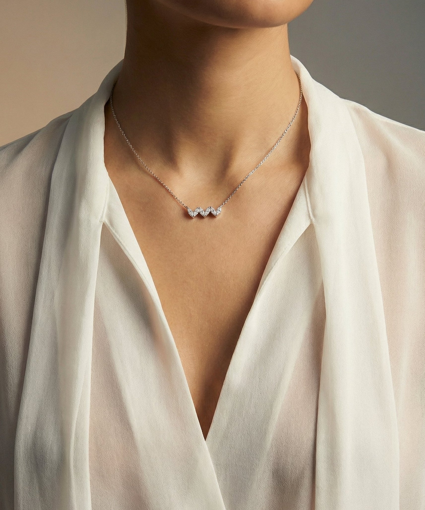 Necklace with three heart-shaped diamonds worn by a person in a white outfit.