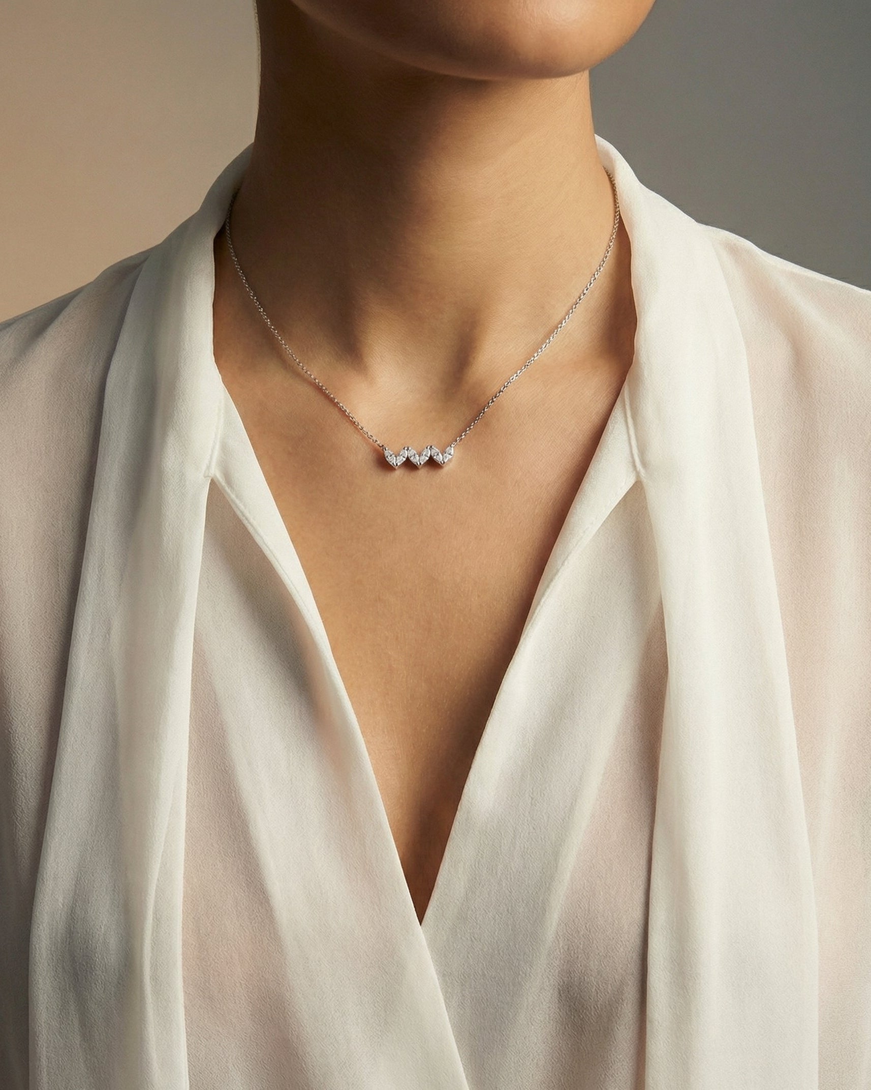Necklace with three heart-shaped diamonds worn by a person in a white outfit.