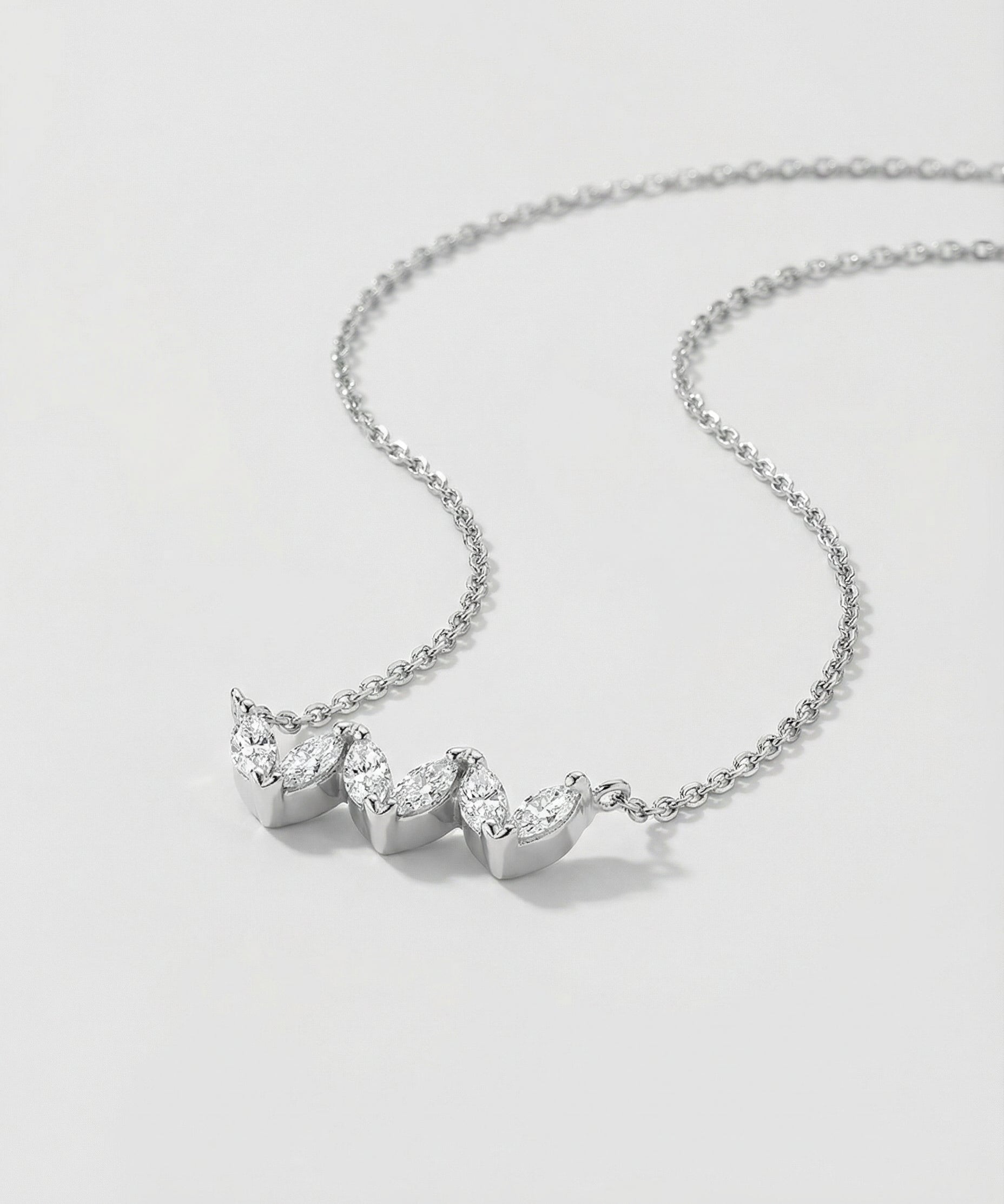 White gold necklace with three heart-shaped gemstones on a light gray background