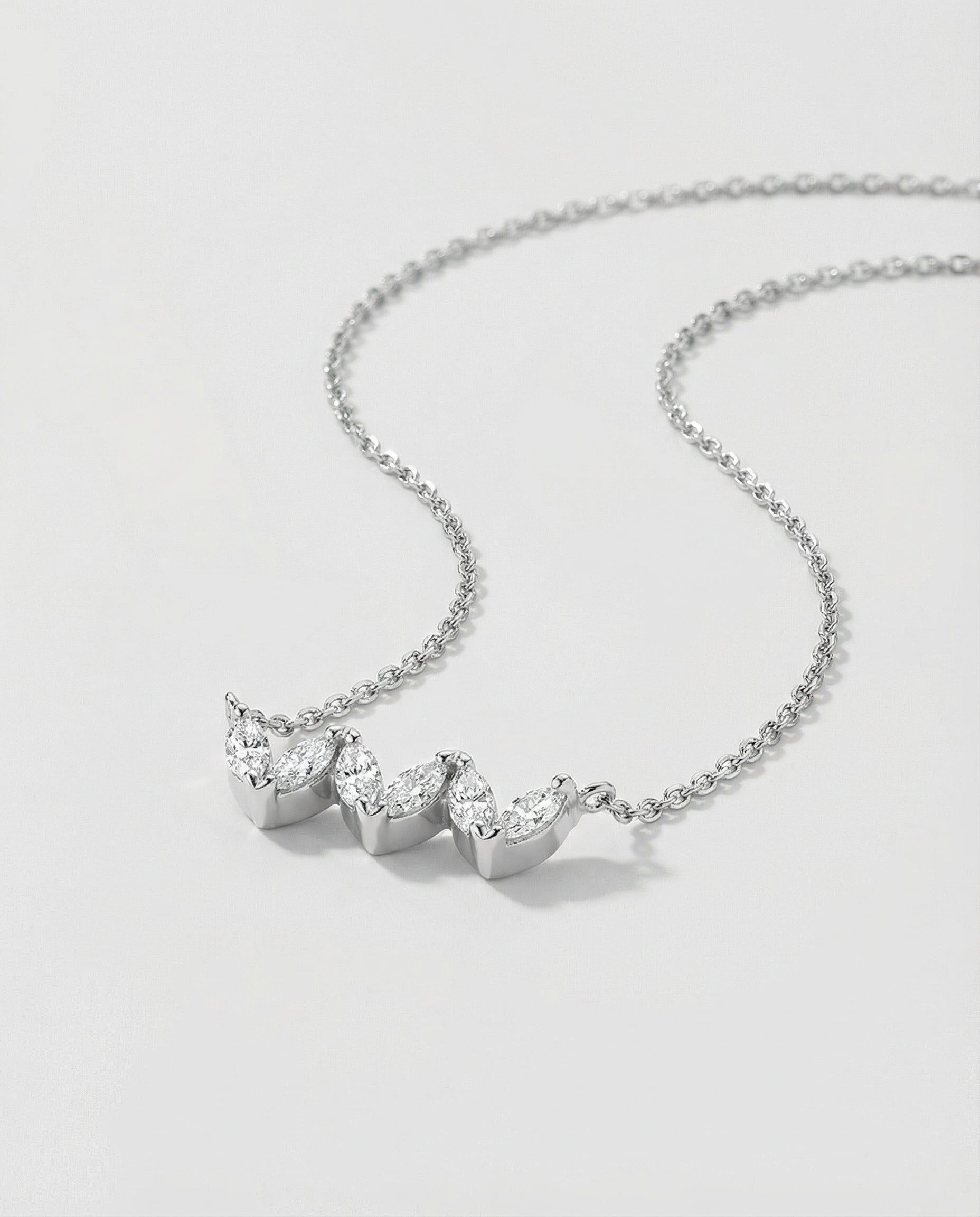 White gold necklace with three heart-shaped gemstones on a light gray background