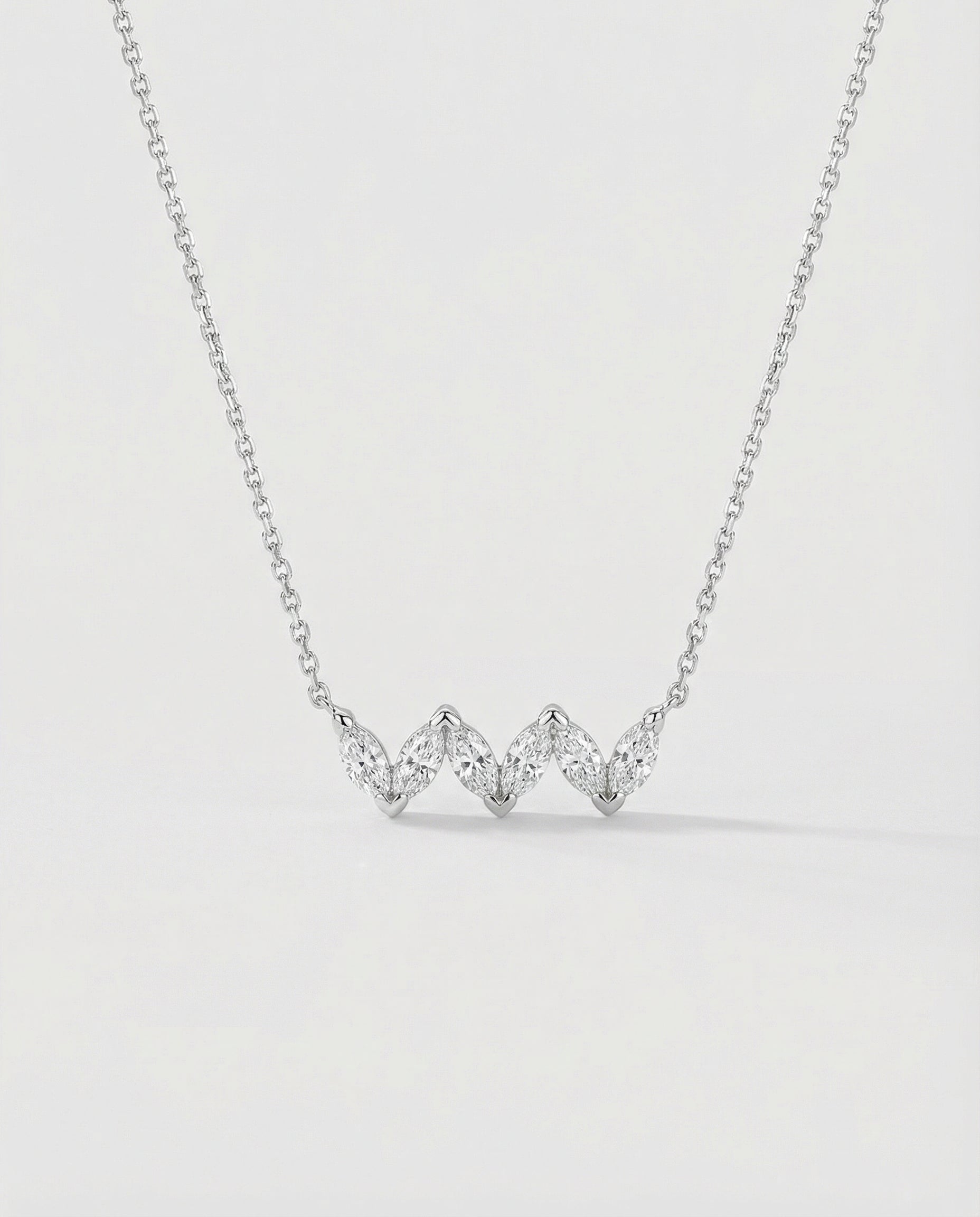 White gold necklace with three heart-shaped diamonds on a light gray background