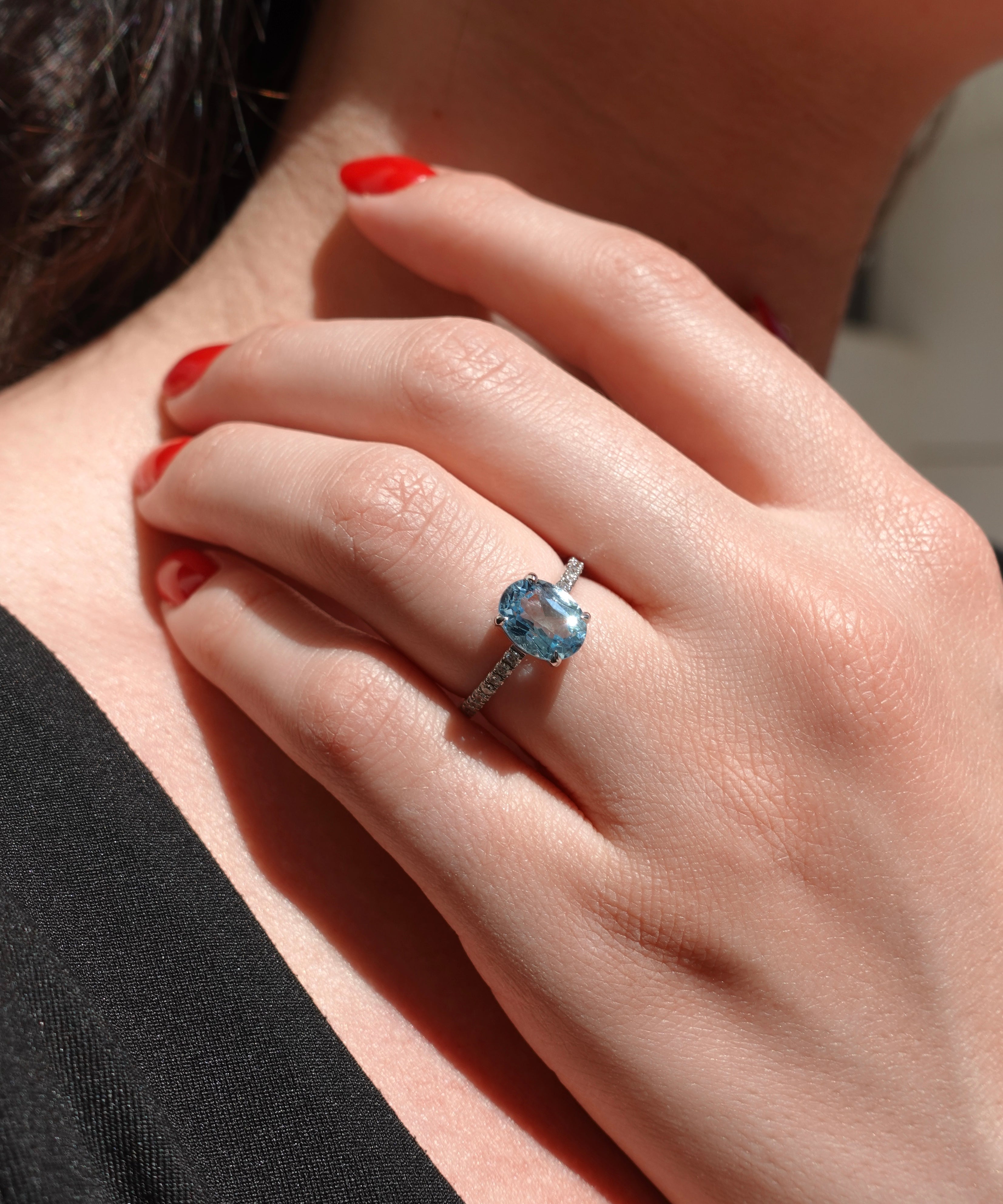 Close-up of a hand wearing a ring with a blue gemstone, against a blurred background.