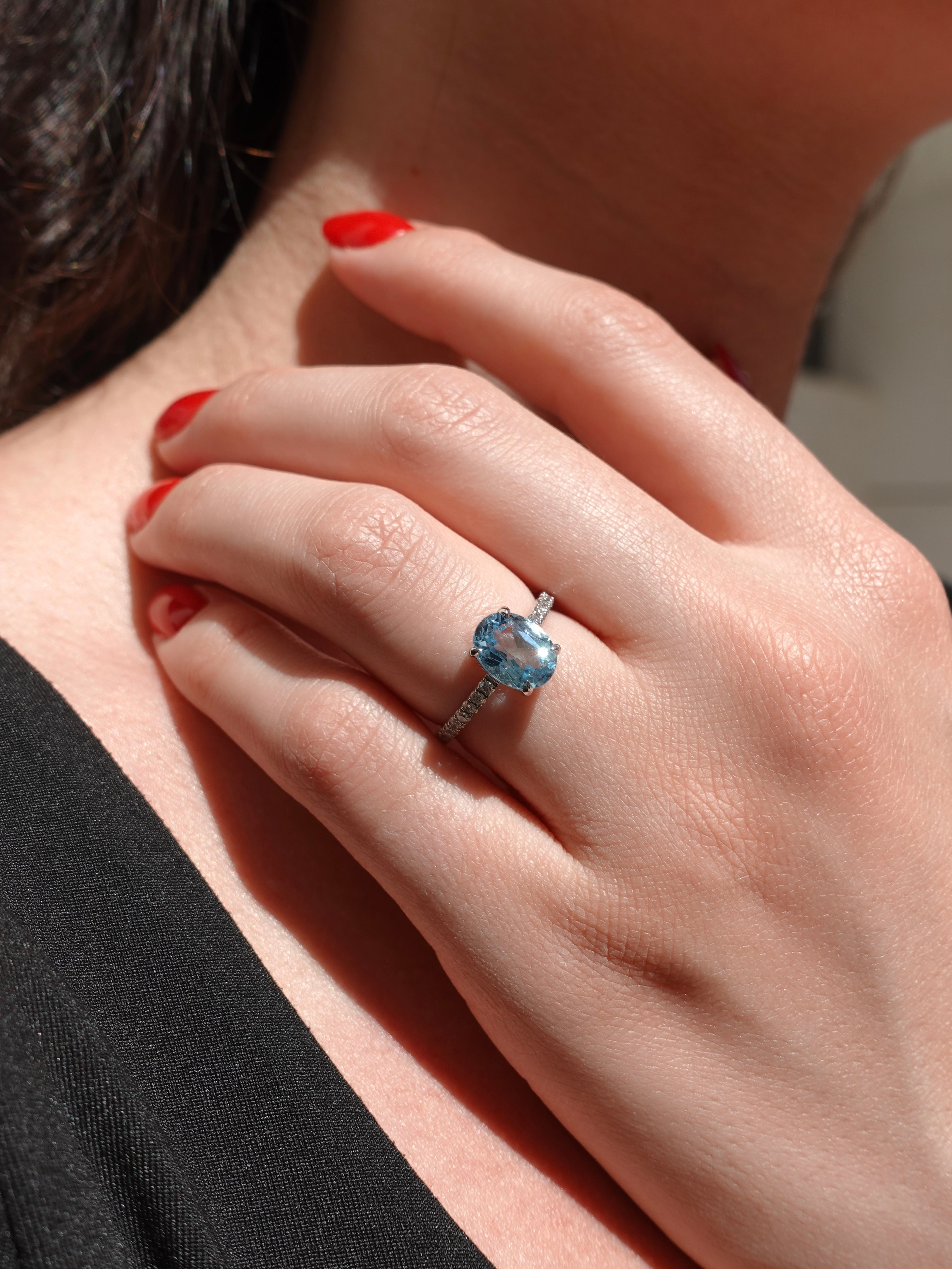Close-up of a hand wearing a ring with a blue gemstone, against a blurred background.