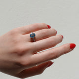 Hand wearing a ring with a blue topaz gemstone on a neutral background