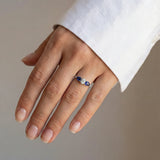 Hand wearing a ring with a central diamond and sapphires on a neutral background