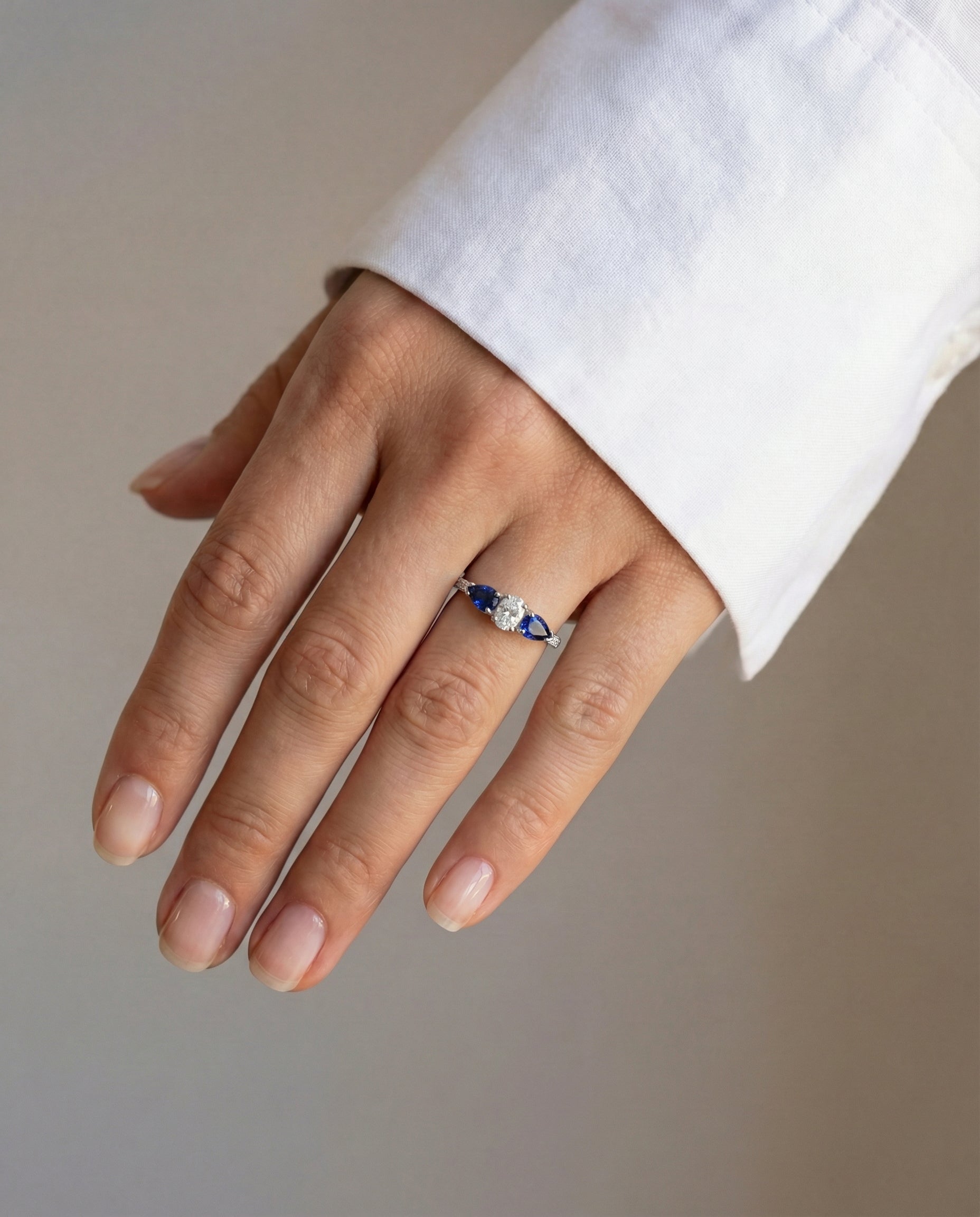 Hand wearing a ring with a central diamond and sapphires on a neutral background