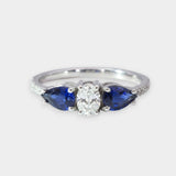 White gold ring with a central diamond and two blue sapphires on a white background