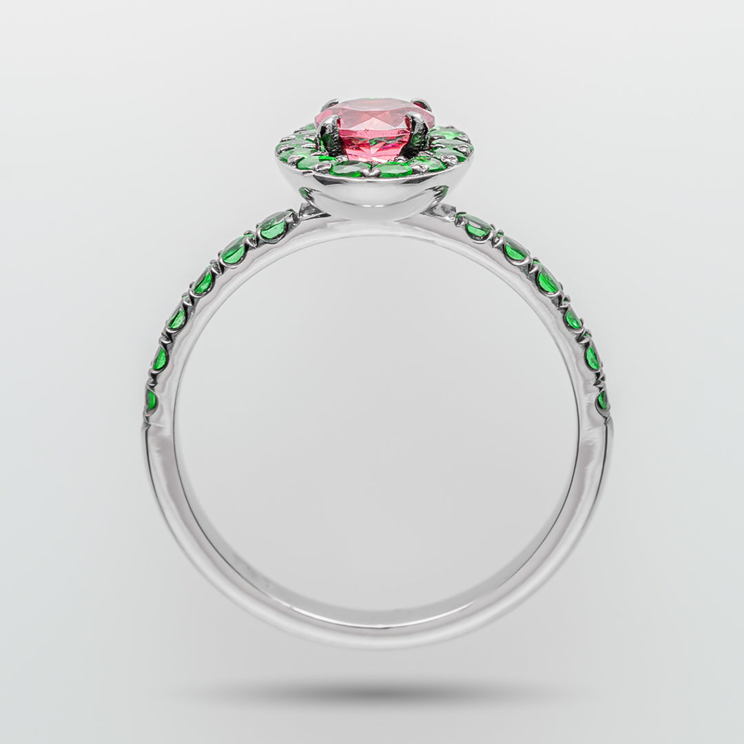 Ring with pink gemstone and green emerald accents on a white background