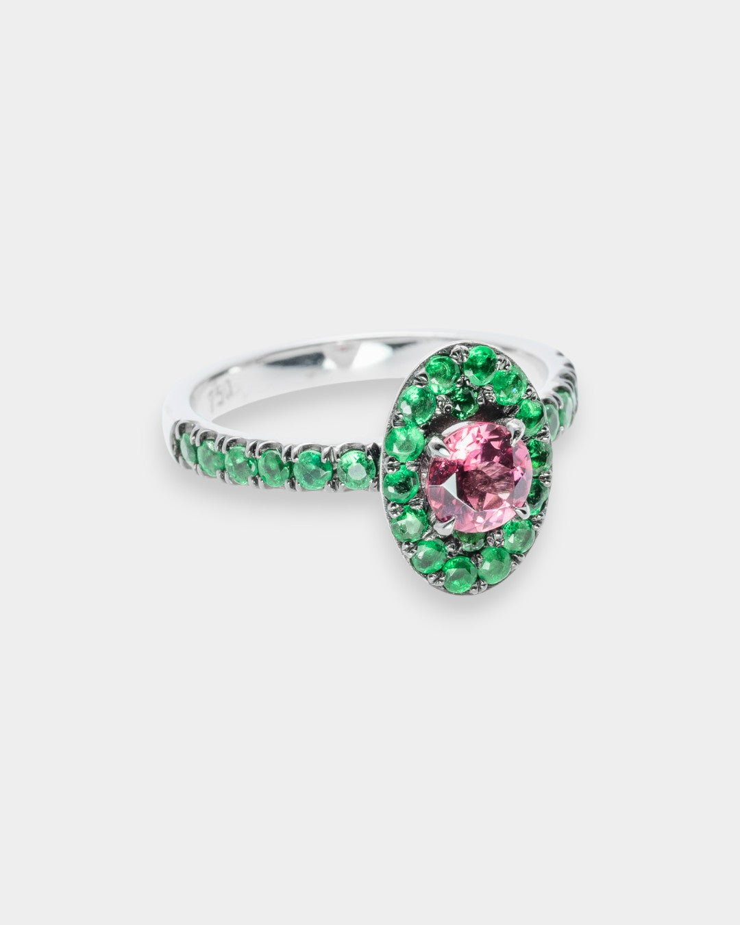 Silver ring with a pink gemstone and green emerald gemstones on a white background