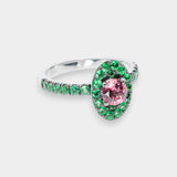 Silver ring with a pink gemstone and green emerald gemstones on a white background