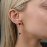 Close-up of a person wearing blue sapphire gemstone earrings with a blurred background