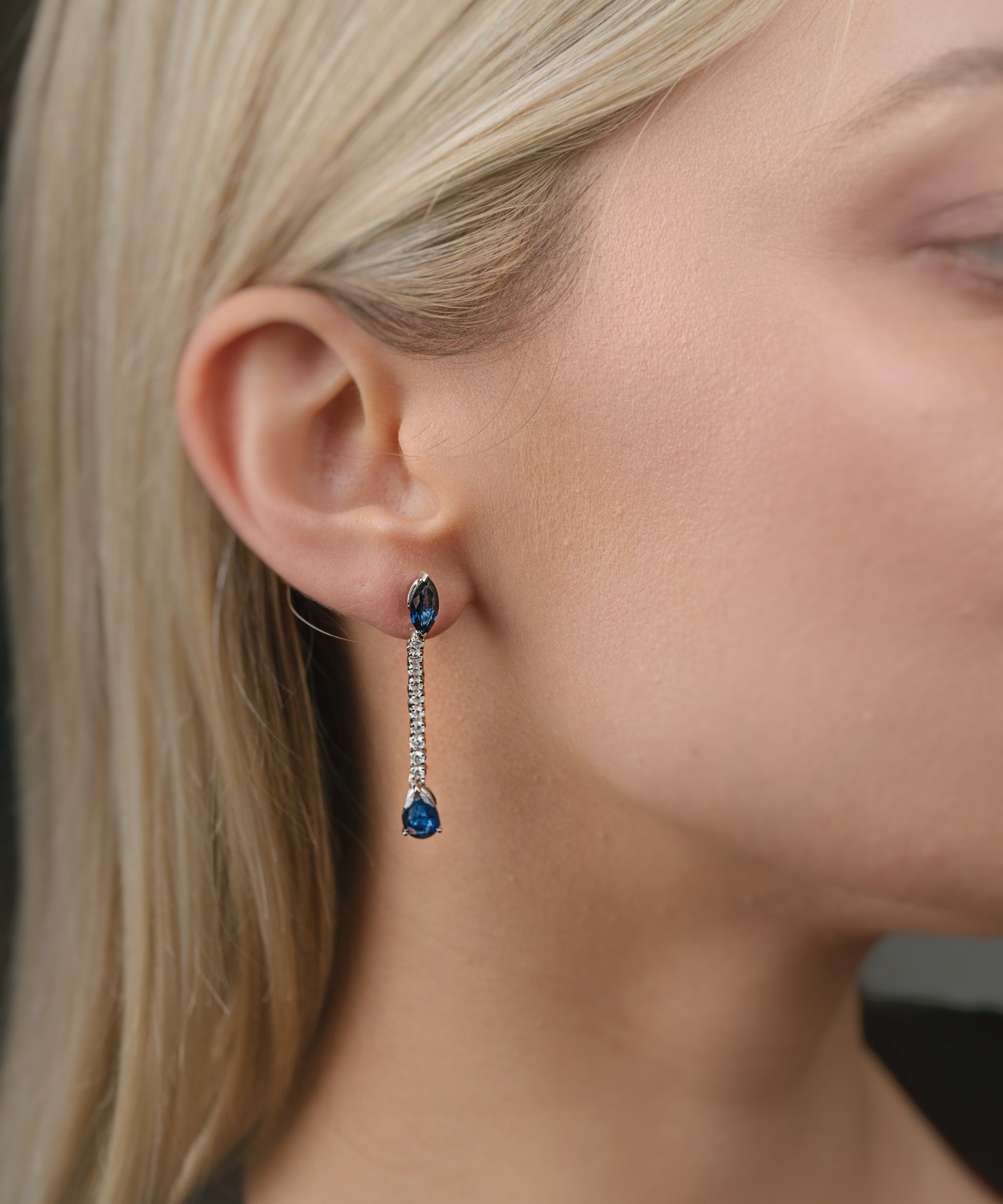 Close-up of a person wearing blue sapphire gemstone earrings with a blurred background