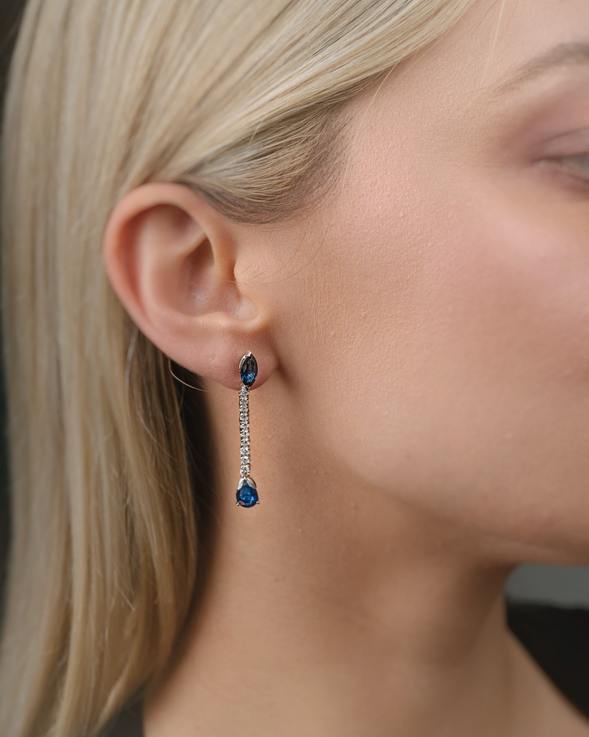 Close-up of a person wearing blue sapphire gemstone earrings with a blurred background