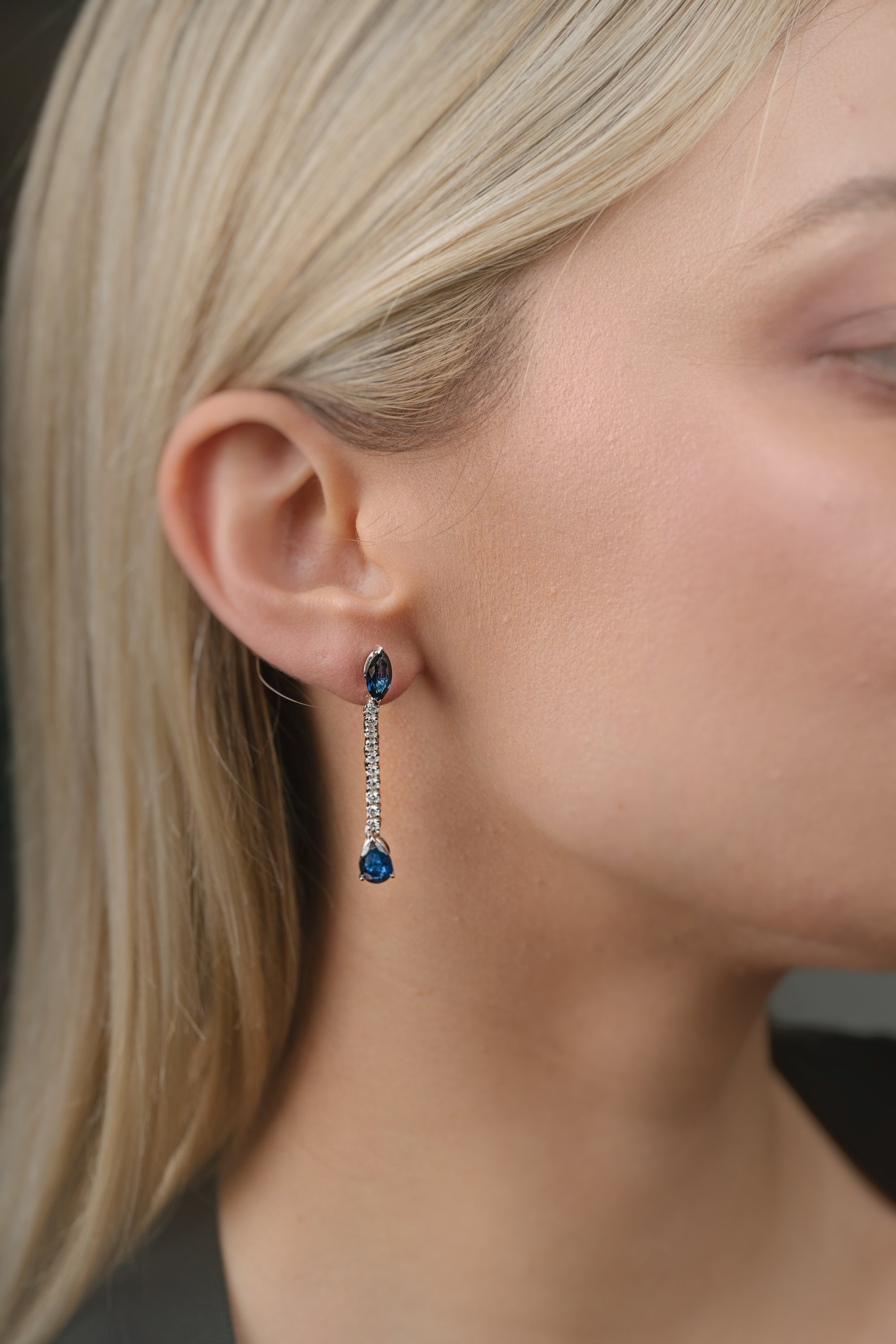 Close-up of a person wearing blue sapphire gemstone earrings with a blurred background