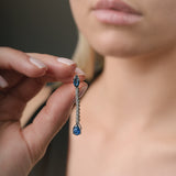 Close-up of a hand holding a blue sapphire gemstone earring near a person's face.