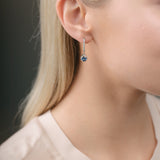 Close-up of a person wearing a diamond earring with sapphire over a dark background