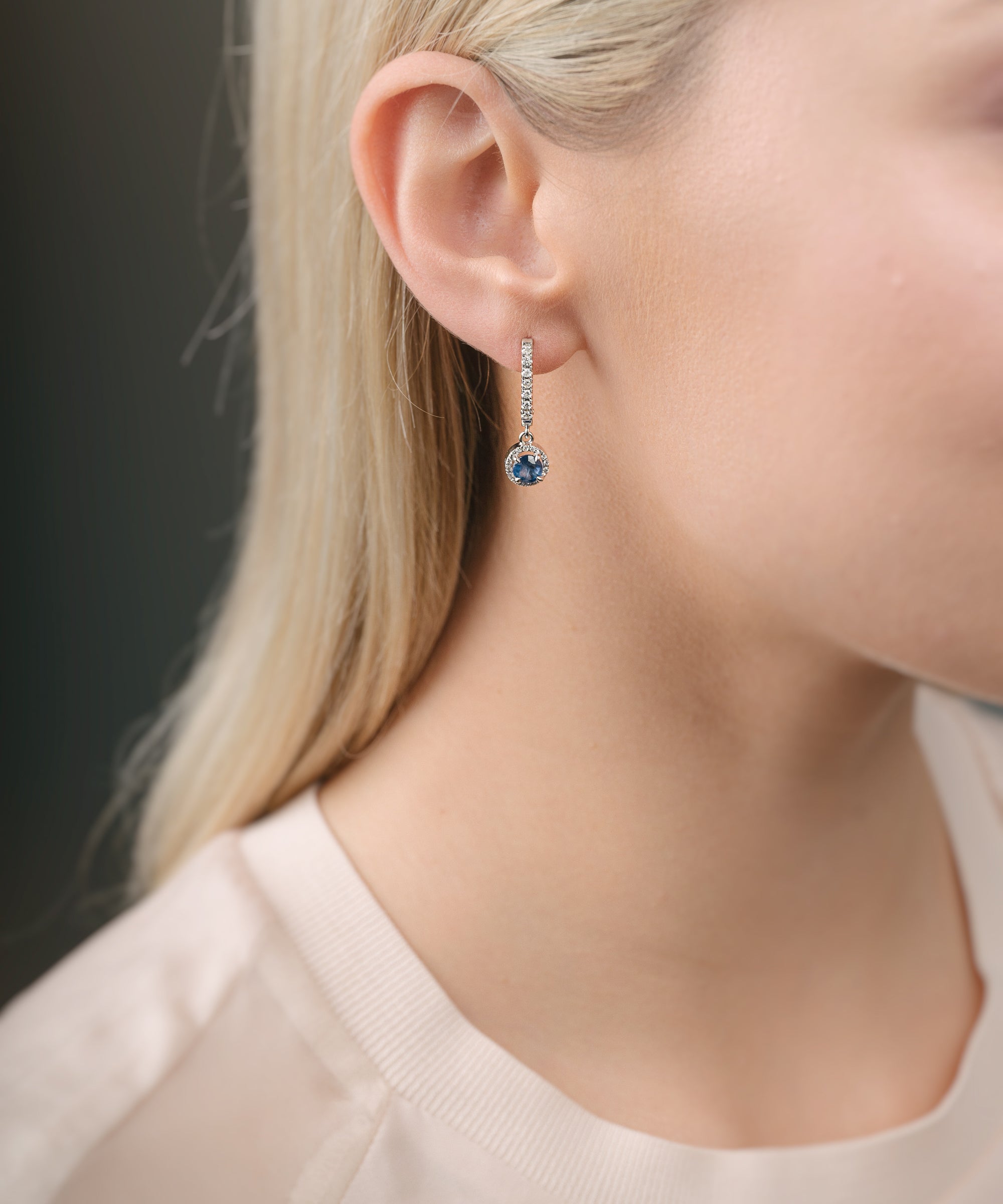 Close-up of a person wearing a diamond earring with sapphire over a dark background