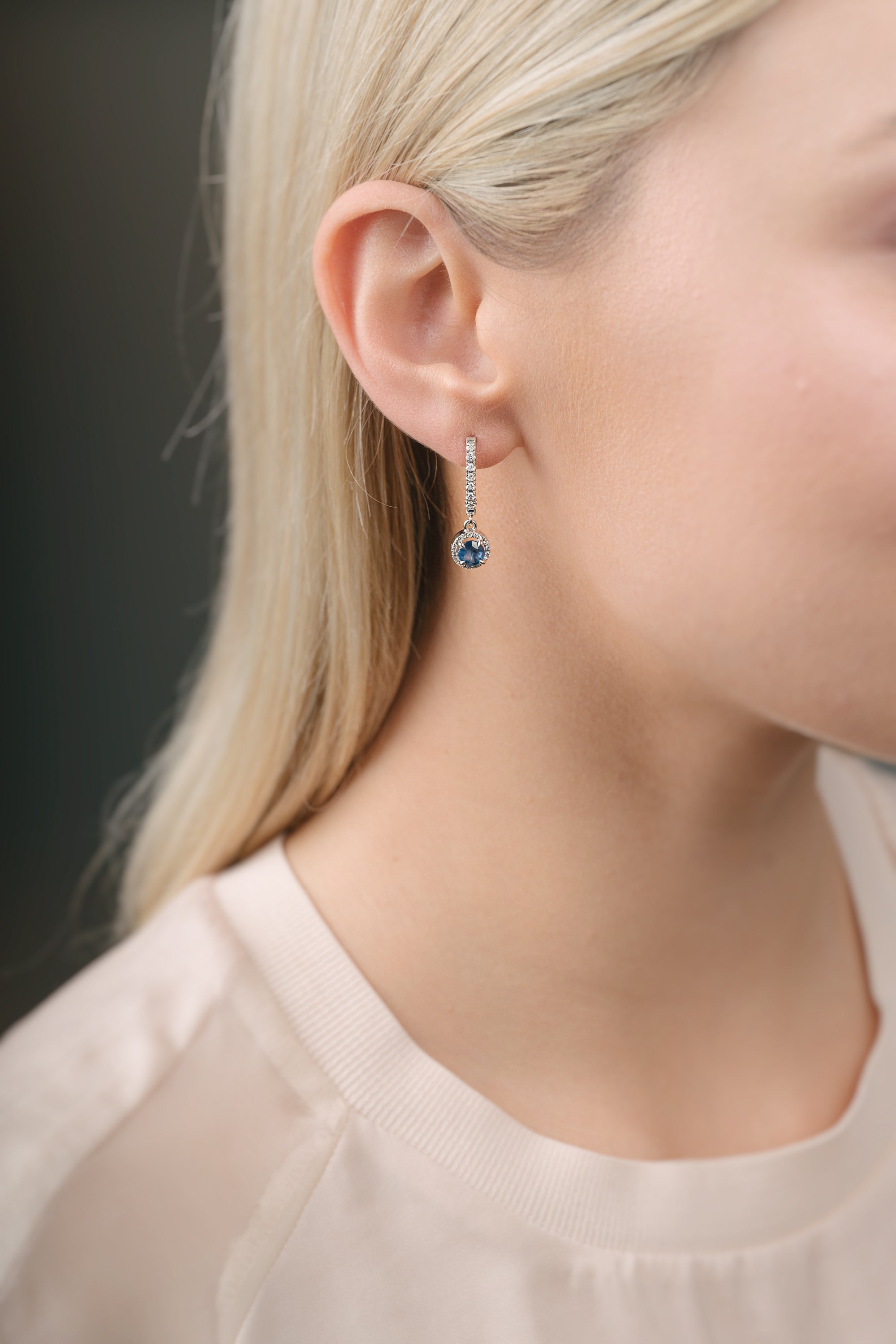 Close-up of a person wearing a diamond earring with sapphire over a dark background