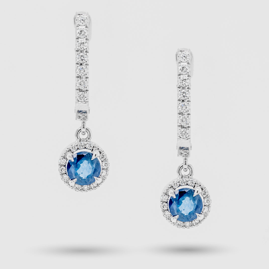Pair of earrings with blue sapphire gemstones and diamond accents on a light gray background