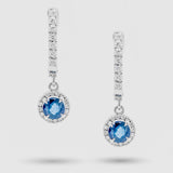 Pair of earrings with blue sapphire gemstones and diamond accents on a light gray background