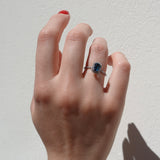 Hand wearing a ring with a blue gemstone on a light background